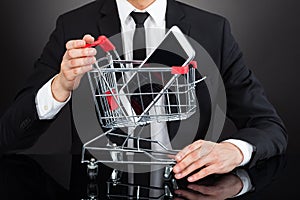 Businessman With Shopping Cart Model And Mobile Phone At Desk