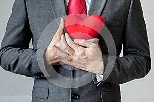 Businessman showing compassion holding red heart onto his chest