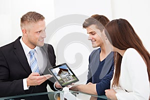 Businessman showing house picture to couple on tablet