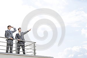 Businessman showing something to coworker against cloudy sky