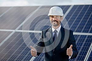 Businessman showing thumbs up, solar panels behind him.