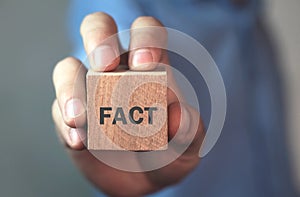 Businessman showing word Fact on wooden cube.