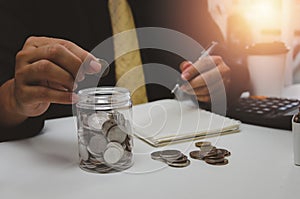 Businessman is shown holding a jar with coins for savings and investments. Concept of tax payments and business accounting