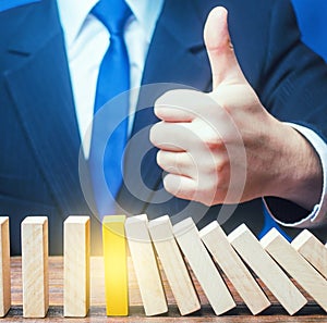 A businessman shows a thumbs up approval over a stopped process falling domino. Achieving success and completing a task. Solution