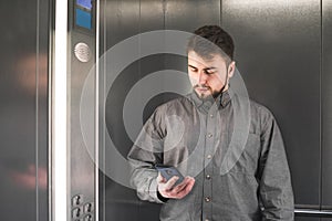 Businessman in the shurt is looking at her smartphone in the lift. Young office worker is surfing the internet by her phone in the