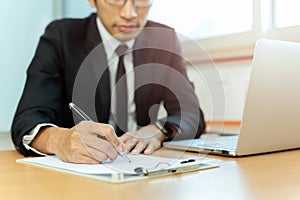 Businessman signing contract paper with pen and laptop in office desk.
