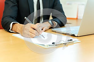 Businessman signing contract paper with pen and laptop in office desk.