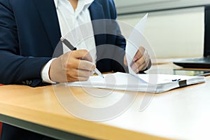 Businessman signing contract paper with pen in office desk.