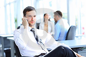 Businessman sit at his desk while talking on mobile in office