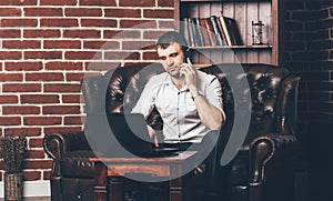A businessman sits on the couch and calls from the phone. Rich man is surrounded by a stylish interior of the room photo