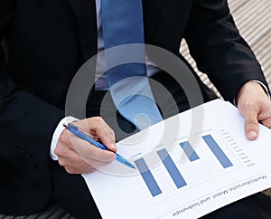 Businessman sits outside on a bench and looks at a chart with blue columns