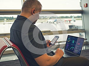 Businessman sitting at airport with laptop and smartphone