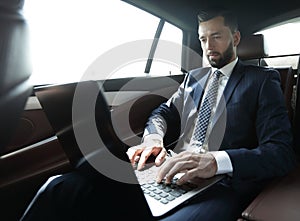 Businessman sitting in the back-seat of a car, using his laptop