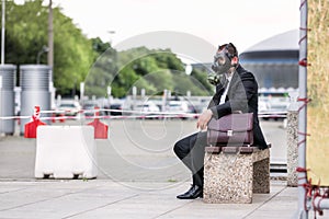 Businessman sitting on a banch with briefcase wearing a gas mask on face