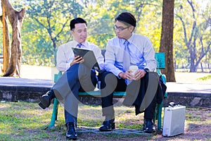 Businessman,They are sitting on bench in park.He is play notebook and  search internet.A