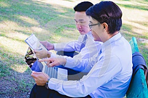 Businessman,They are sitting on bench in park.He is play notebook and  search internet.A