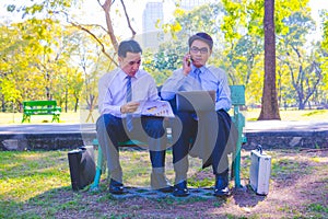 Businessman,They are sitting on bench in park.He is play notebook and  search internet.A