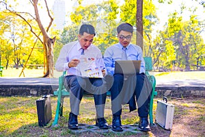 Businessman,They are sitting on bench in park.He is play notebook and  search internet.A