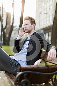 Businessman sitting on a bench and talking on the phone on a s