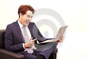 A Businessman sitting on the black sofa, happily pose, pointing his finger at the monitor of laptop computer after checking