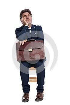 Businessman sitting with briefcase on laps looking up pensive