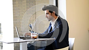 Businessman sitting in cafe, drinking fresh coffee typing with his laptop.