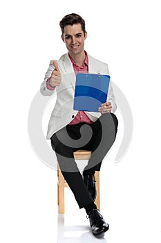 Businessman sitting on chair holds a notepad and makes ok