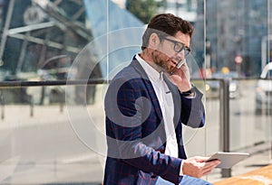 Businessman sitting in the city using a tablet and cellphone