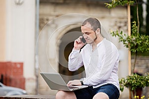 Businessman sitting in citypark using mobilephone and laptop.