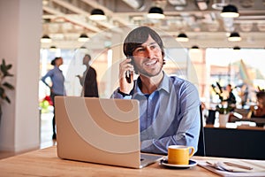 Businessman Sitting At Desk On Phone Call In Modern Open Plan Office