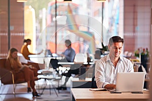 Businessman Sitting At Desk Working On Laptop In Modern Open Plan Office