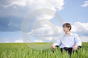 Businessman sitting on grassland under blue sky