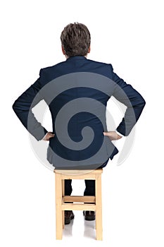 Businessman sitting with hands on waist intrigued