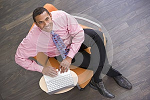 Businessman sitting indoors with laptop smiling