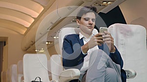 Businessman sitting inside plane watching video on mobile phone during his business trip