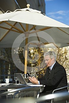 Businessman sitting with laptop and dialing cellphone.