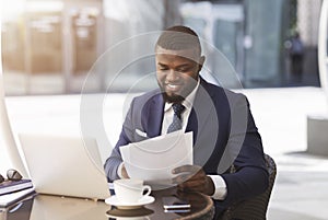 Businessman Sitting At Laptop Working With Papers In Outdoor Cafe