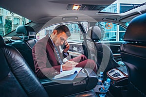 Businessman sitting in a limo while talking on his phone reading his notes and planning his day photo