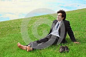 Businessman sitting on the meadow barefoot