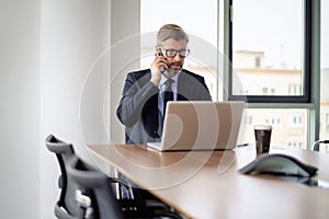 Businessman sitting in a modern office and using mobile phone and laptop for work