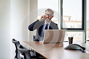 Businessman sitting in a modern office and using mobile phone and laptop for work