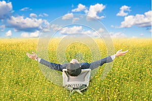 Businessman sitting on office armchair and open arm in yellow flower field