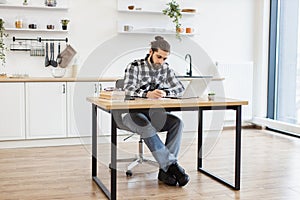 Businessman sitting at office desk with digital devices in spacious dining room.