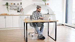 Businessman sitting at office desk with digital devices in spacious dining room.