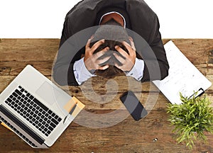 Businessman sitting at office desk with hands on his head crying devastated and frustrated