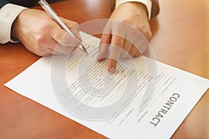 Businessman sitting at office desk signing a contract with shallow focus on signature