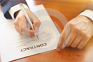 Businessman sitting at office desk signing a contract with shallow focus on signature