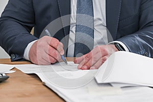 Businessman sitting at office desk signing contract with shallow focus on signature. Head of company sign contract