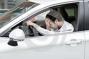 Businessman sitting in own car stuck in traffic, holding his hand on forehead and nervously waiting