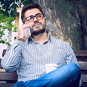 Businessman sitting on park bench with coffee using mobile phone.